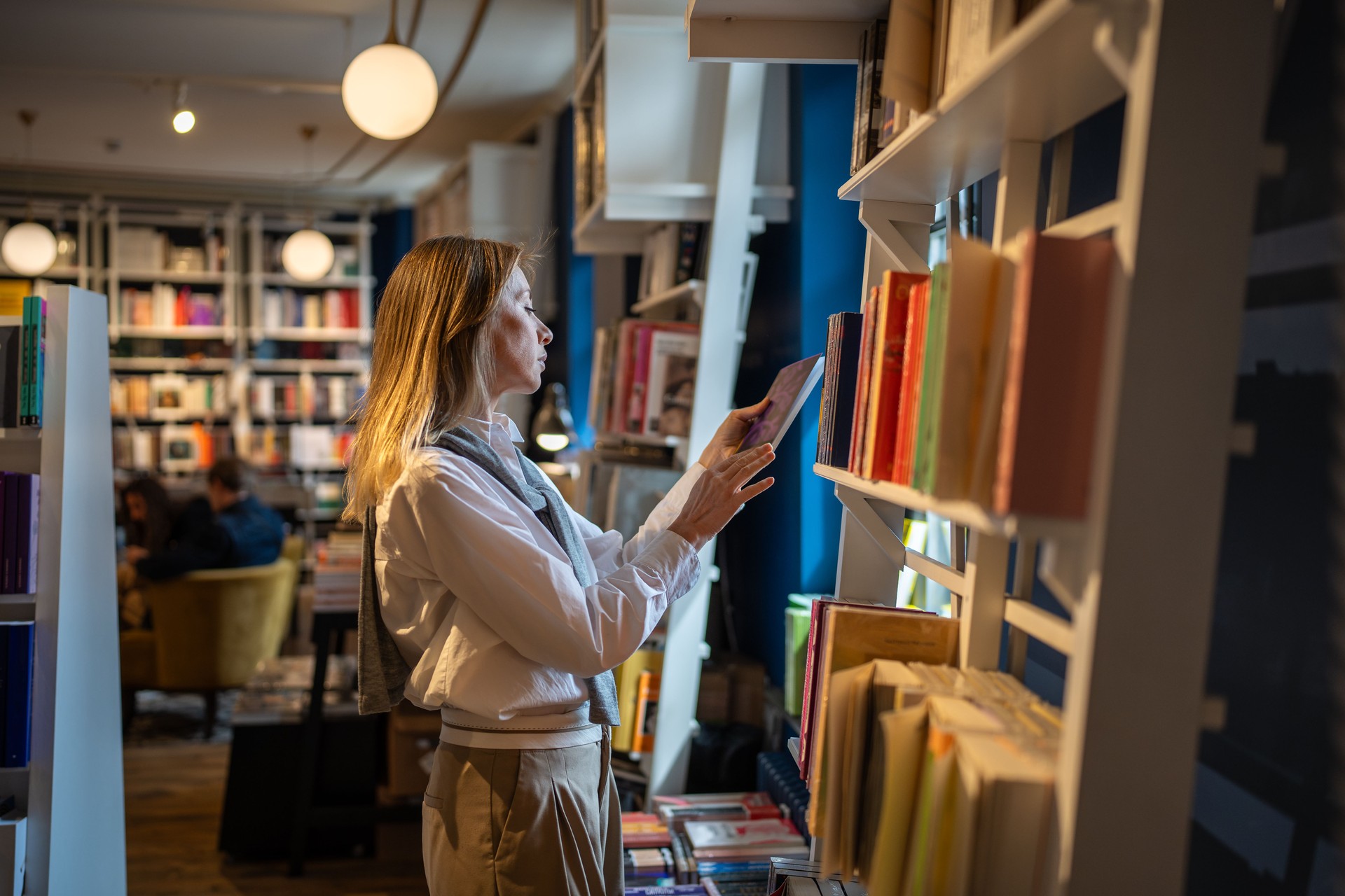 Thoughtful woman customer chooses and reads books from shelves in bookshop. Book worm and read hobby